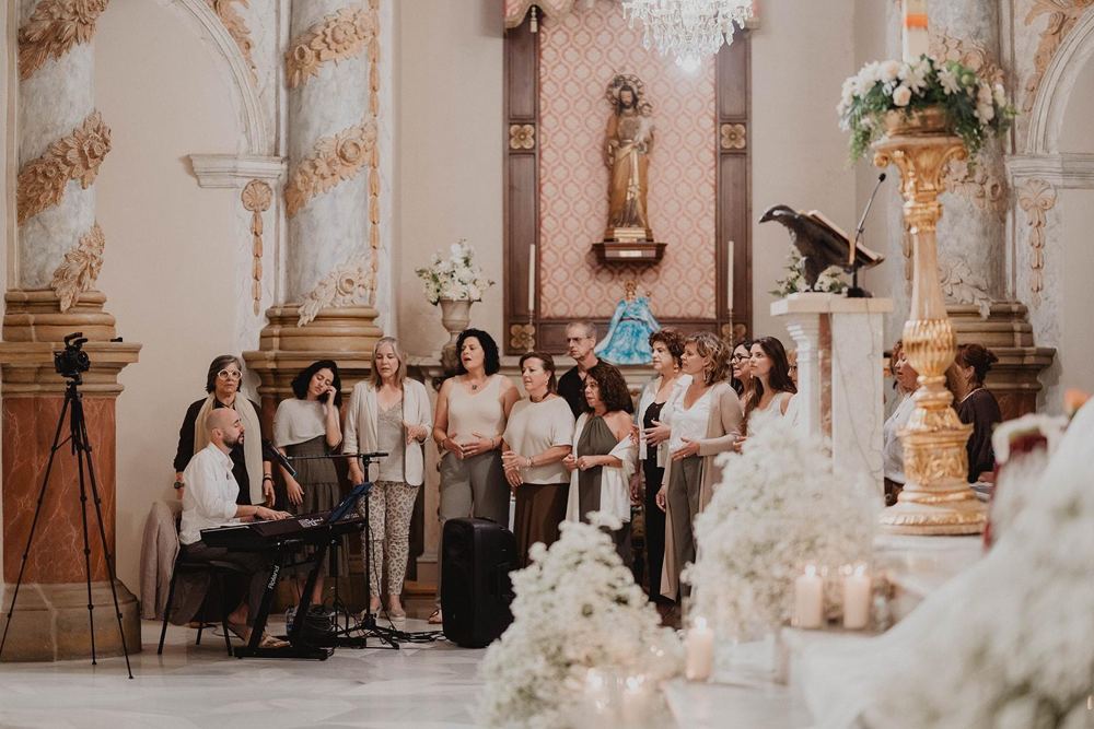 El coro cantando en una boda dentro de una iglesia decorada con flores blancas