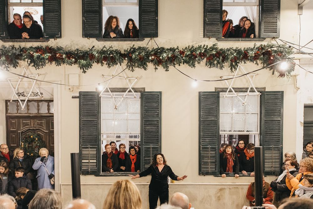El coro cantando desde las ventanas de una casa decorada por Navidad